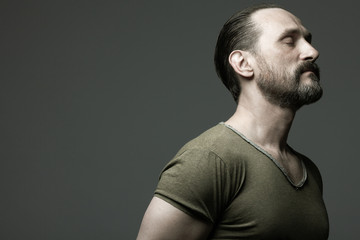 Fabulous at any age. Profile portrait of charismatic muscular 40-year-old man standing over dark gray background. Hair brushed back. Rocker, biker style. Close up. Copy-space. Studio shot © Augustino