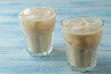 iced coffee with milk and ice cubes in a glass cup on a light blue background. refreshing drink. summer drink.
