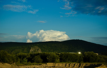 Cloudy blue sky on the horizon of Russian fields and mountains. Summer forest on a sunny day.