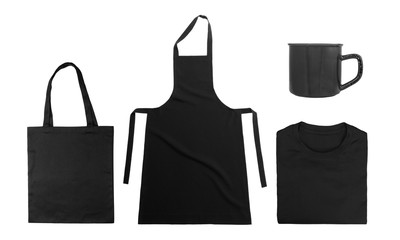 Collection of black objects isolated on white background. Black cotton bag, black folded t-shirt, kitchen apron, metal mug. Flat lay. Top view