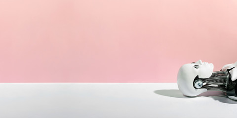 Closeup of abstract white robot lying down on white surface against pink background with copy space © Dmitry Zimin
