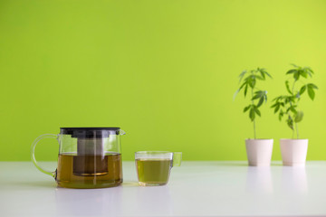 White table with Marijuana plant in pottery. Hot CBD tea in glass and teapot.