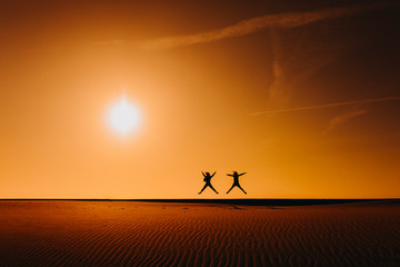 silhouette of two women friends jumping at the beach at sunset during golden hour. Fun and friendship outdoors