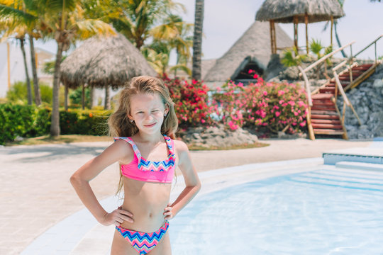 Little girl with bottle of sun cream in swimming pool