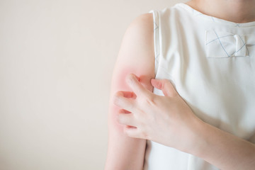 Young woman scratching arm from having itching on white background w/ copy space. Cause of itchy...