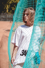 Stylish modern woman In white T-shirt with the inscription Sunset in Russian language - poses on sports ground. Grid on the tennis court.