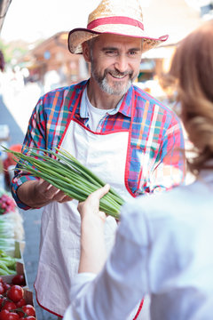 Happy Senior Farmer Selling Organic Vegetables In A Farmer's Marketplace. Serving Mature Female Customer. Healthy Organic Local Food Production