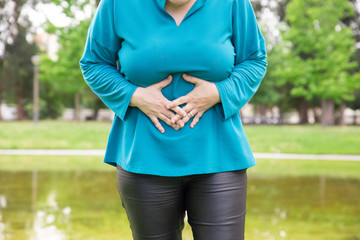 Woman suffering from belly ache. Plus sized lady standing in park and touching stomach. Health...