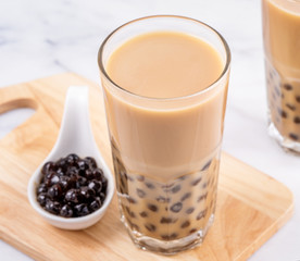 Popular Taiwan drink - Bubble milk tea with tapioca pearl ball in drinking glass on marble white table wooden tray background, close up, copy space