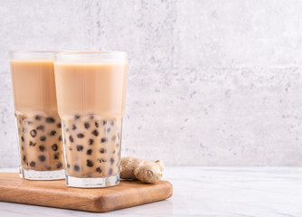 Popular Taiwan drink - Bubble milk tea with tapioca pearl ball in drinking glass on marble white table wooden tray background, close up, copy space