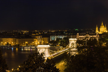 Budapest urban scape with the Basilica, Devil's Wheel and the illuminated Chain Bridge across the Danube River by night.