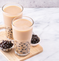 Popular Taiwan drink - Bubble milk tea with tapioca pearl ball in drinking glass on marble white table wooden tray background, close up, copy space
