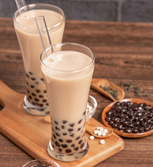 Popular Taiwan drink - Bubble milk tea with tapioca pearl ball in drinking glass and straw, wooden table gray brick background, close up, copy space