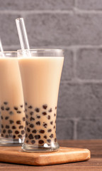 Popular Taiwan drink - Bubble milk tea with tapioca pearl ball in drinking glass and straw, wooden table gray brick background, close up, copy space