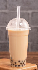 Takeout with disposable item concept popular Taiwan drink bubble milk tea with plastic cup and straw on wooden table background, close up, copy space