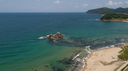 Obraz premium aerial footage of blue ocean, white wave and the twin rocks through the torii gate at the coast of sakurai futamigaura beach, itoshima fukuoka japan