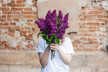 Woman holding a vivid bunch of lilac flowers against brick wall