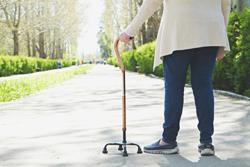 Senior disabled caucasian woman hands on cane outside nursing home park. Close up of elderly lady...