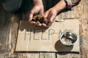 Male beggar hands seeking money with sign HELP ME from human kindness on the wooden floor at public path way or street walkway. Homeless poor in the city. Problems with finance, place of residence.