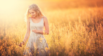 Fototapeta na wymiar Beautiful tender blonde young girl standing at summer meadow in gray sundress. Free happy woman enjoying nature.