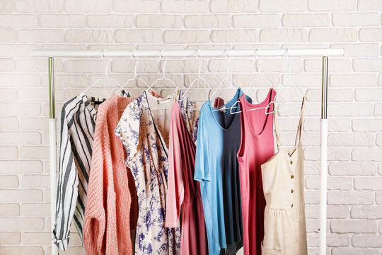 Women's hip clothing store interior concept. Row of different colorful female clothes hanging on rack in hipster fashion show room in shopping mall. White brick wall background. Copy space.