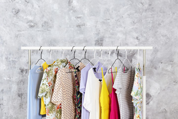 Women's hip clothing store interior concept. Row of different colorful female clothes hanging on rack in hipster fashion show room in shopping mall. Grunged concrete wall background. Copy space.