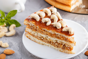 Piece of homemade cake with caramel cream and nuts with cup of coffee on a gray concrete  background, side view.