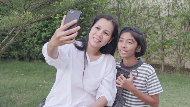 Asian mother and daughter selfie by smartphone together in the garden at home. A girl and women are smile when taking picture on garden background
