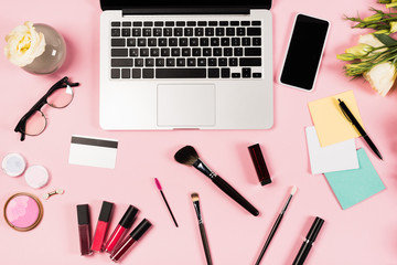 top view of laptop, smartphone with blank screen, credit card, glasses, flowers and decorative cosmetics on pink