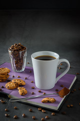 Black hot coffee with steam in a white coffee cup, placed on a book with cookies  with a loft-style background.