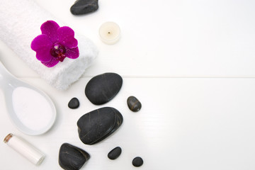 Spa setting with pink orchids, black stones and bath salts .