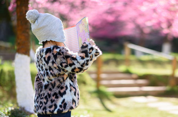 Asian child tourists holding a map in the park full of cherry blossoms