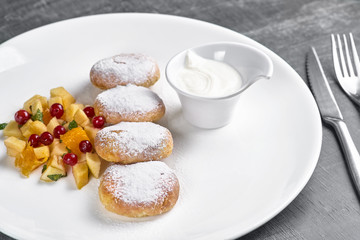 Healthy breakfast Russian cheese curd pancakes with fruit and sour cream for breakfast on a dark wooden background.