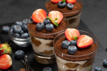 Classic tiramisu dessert with blueberries and strawberries in a glass on dark concrete background