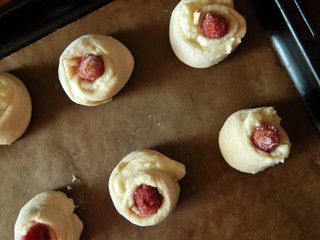 Raw custard buns with fresh strawberries on a baking sheet are ready to be baked. Homemade bakery concept.
