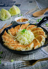 Gyoza fried dumplings in hot saucepan, soy sauce and chopsticks on the plate