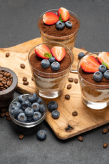 Classic tiramisu dessert with blueberries and strawberries in a glass on dark concrete background