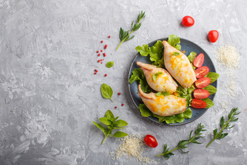 stuffed baked squid with greens on a blue ceramic plate on a gray concrete background, top view.