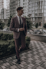 Businessman. Confident young man in full suit adjusting his sleeve and looking away while standing outdoors with cityscape in the background