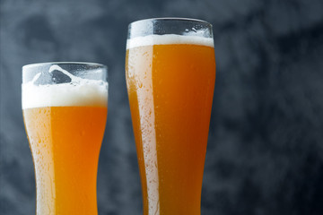 Two glasses of unfiltered cold wheat craft beer on a dark table