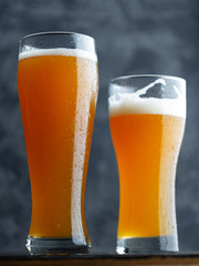 Two glasses of unfiltered cold wheat craft beer on a dark table