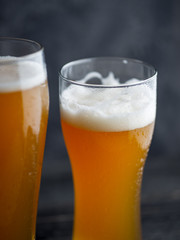 Two glasses of unfiltered cold wheat craft beer on a dark table