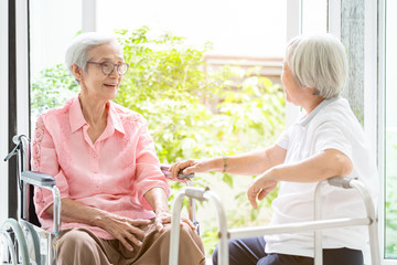 Happy asian senior woman sitting on wheelchair,sister or friend with walker having...