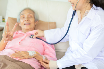 Medical female doctor or nurse checking senior patient using stethoscope in hospital,closeup hand of elderly asian woman showing two fingers,v-sign,feel so happy and smile,health care,support concept