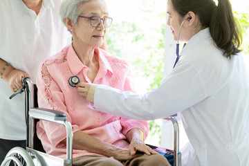 Family asian doctor or smiling nurse checking,listening senior patient’s chest through stethoscope during home visit ,female caregiver examining elderly woman in wheelchair,healthcare,checkup concept.