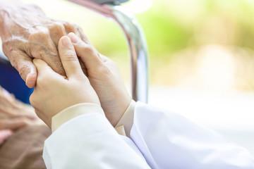 Closeup of hand medical female doctor or nurse holding senior patient hands and comforting her,.Caring caregiver supporting disabled elderly people on wheelchair in hospital,help,health care concept
