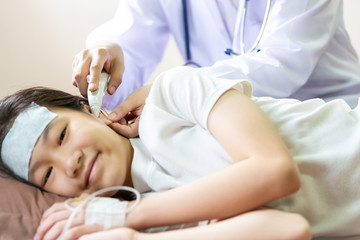 Obraz na płótnie Canvas Doctor or nurse checking child patient temperature in the ear using digital thermometer,asian girl having fever using cold gel placed on her forehead to relief fever,headache, illness in bed hospital