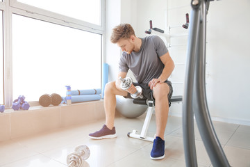 Sporty young man training with dumbbells in gym