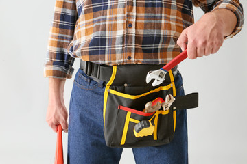 Plumber with tools belt on light background, closeup