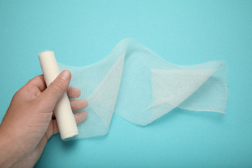 Doctor's hand is holding white gauze bandage on blue background. First aid, injury treatment.